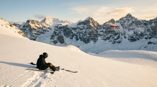 Un skieur blessé allongé dans la neige profonde hors-piste avec un hélicoptère de secours en arrière-plan