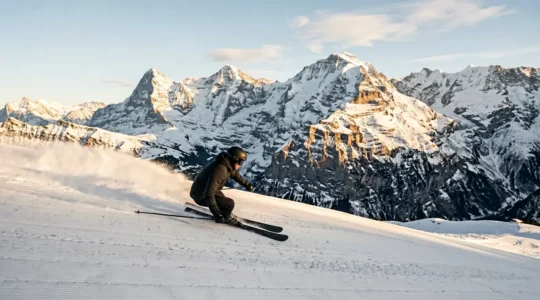 Skieurs en pleine descente exécutant un virage carving parfait sur une piste damée avec vue sur les sommets alpins