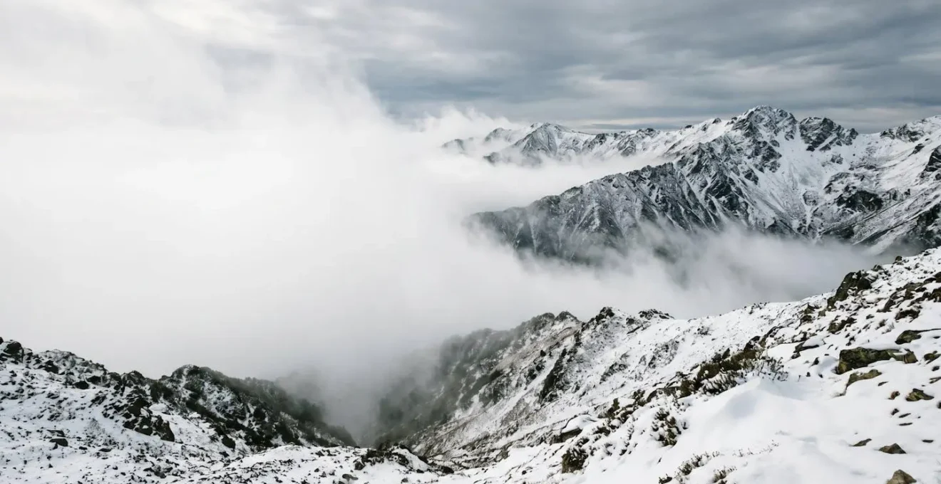 Paysage de montagne enneigé avec nappes de brouillard masquant progressivement les sommets