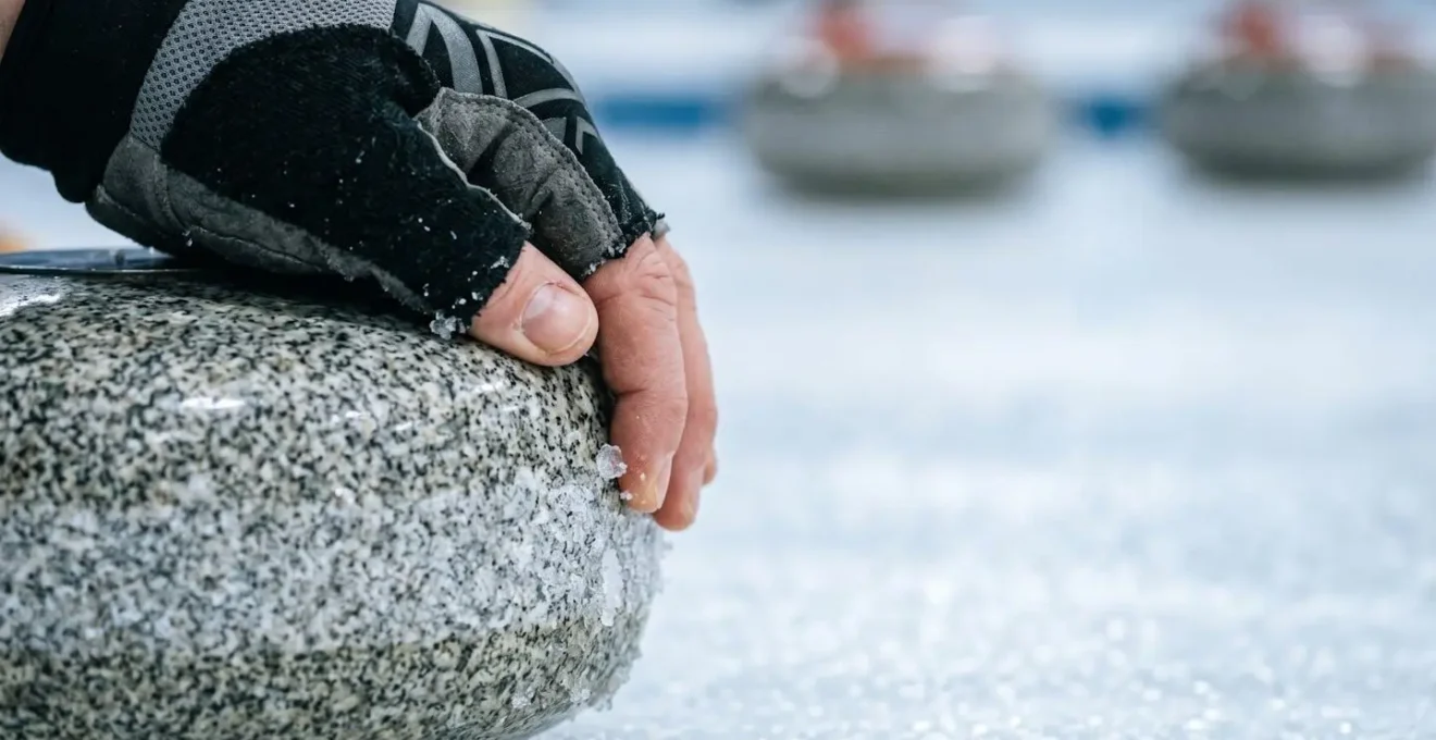 Gros plan sur la main d'un curleur relâchant délicatement une pierre de granite avec effet de rotation visible